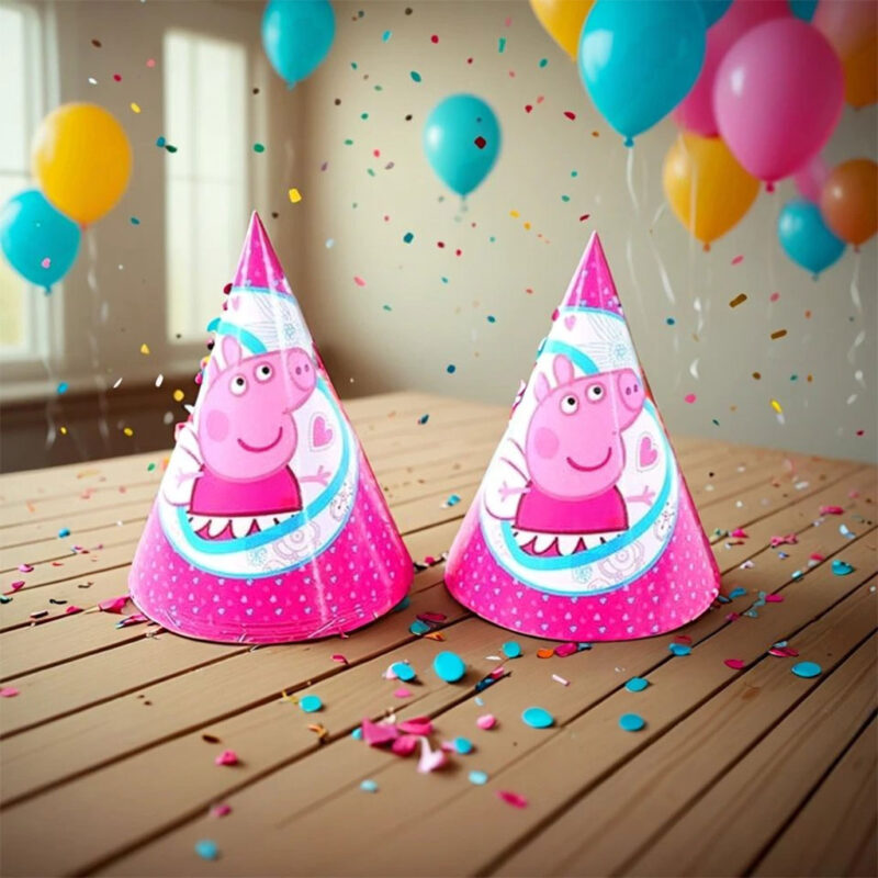 Two Peppa Pig theme birthday hats sitting on a wooden surface with balloons and confetti in the background.