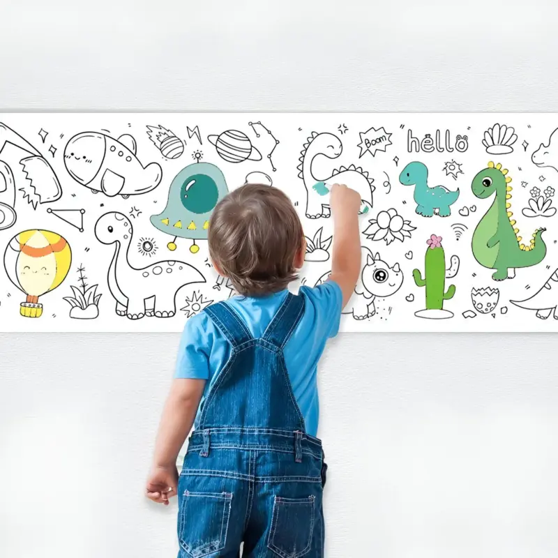 A young child in overalls coloring on a roll of Coloring Wall Paper adhered to a white wall, depicting outlined dinosaurs and hot air balloons.