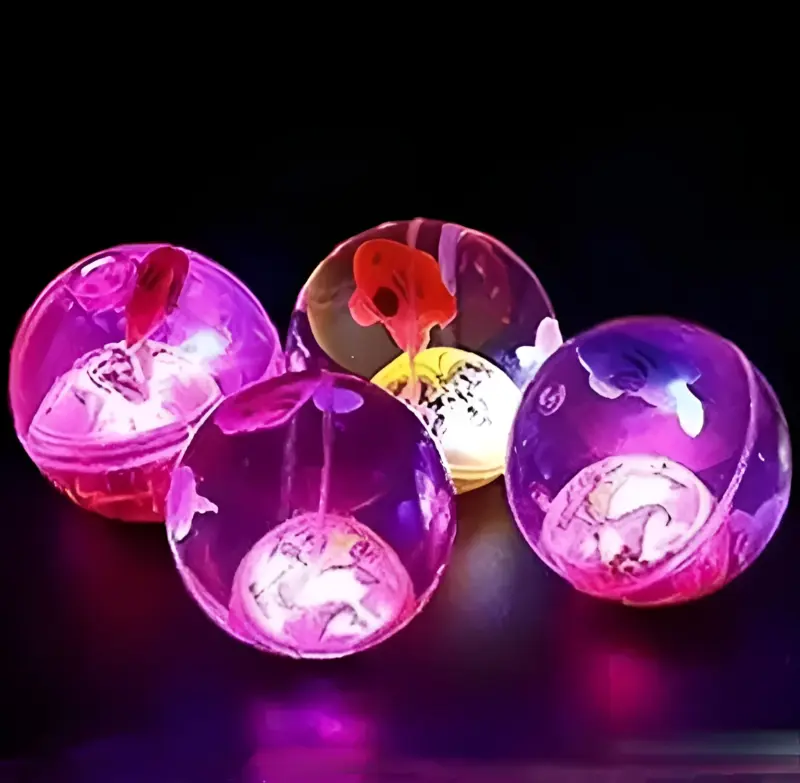 A group of glowing, translucent LED Bounce Balls in purple and pink hues, showing internal light and designs, against a dark background.