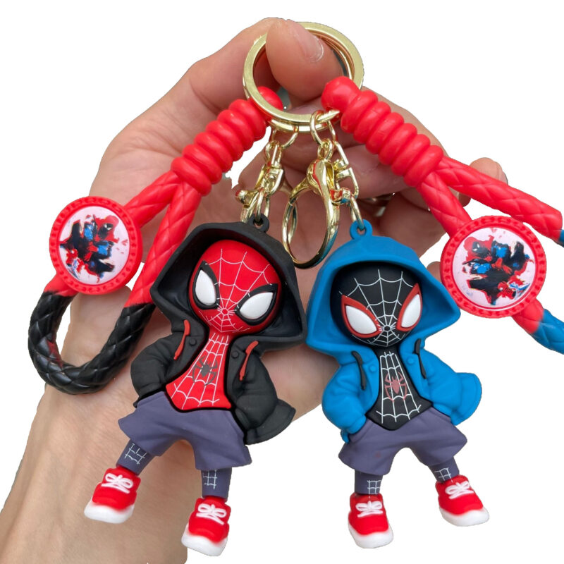 A hand holding two Spiderman Keychains: one red and black, and one blue and black, both featuring chibi-style Spiderman characters in hoodies with braided straps.