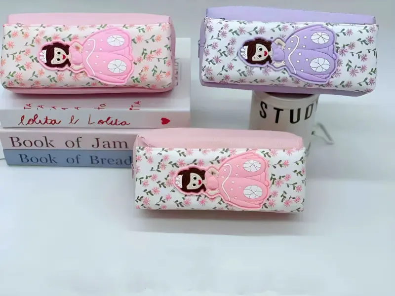 Three Doll Pouches in pink and lavender, featuring a 3D doll figure with butterfly wings and a floral pattern, stacked on books.